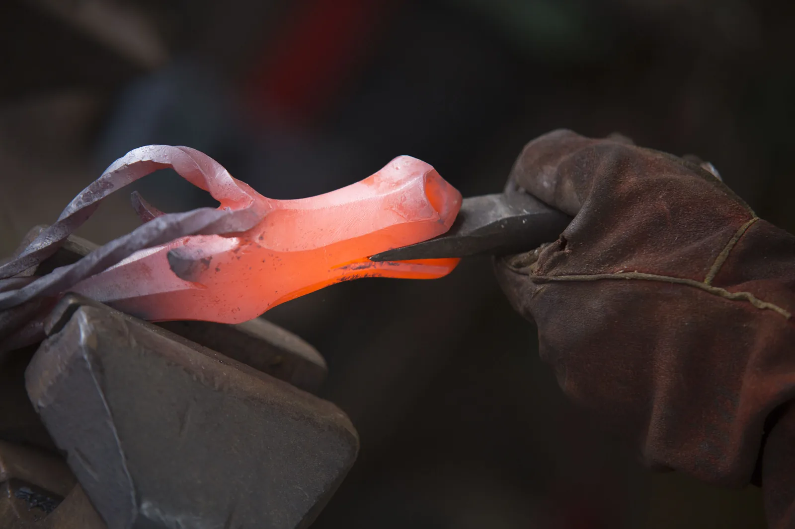 Glowing hot iron being shaped with tongs at the forge